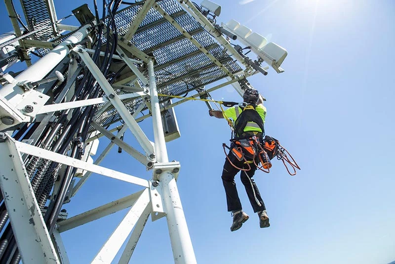 Worker climbing telecommunications tower with Ergodyne harness and Pryme safety solutions in Australia.