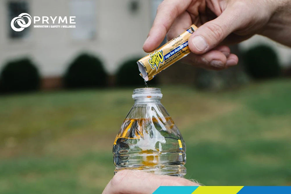 Worker pouring Sqwincher electrolyte powder into a water bottle for on-site hydration.