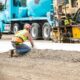 Construction worker wearing Ergodyne ProFlex back support belt while kneeling at a worksite for heavy lifting safety.