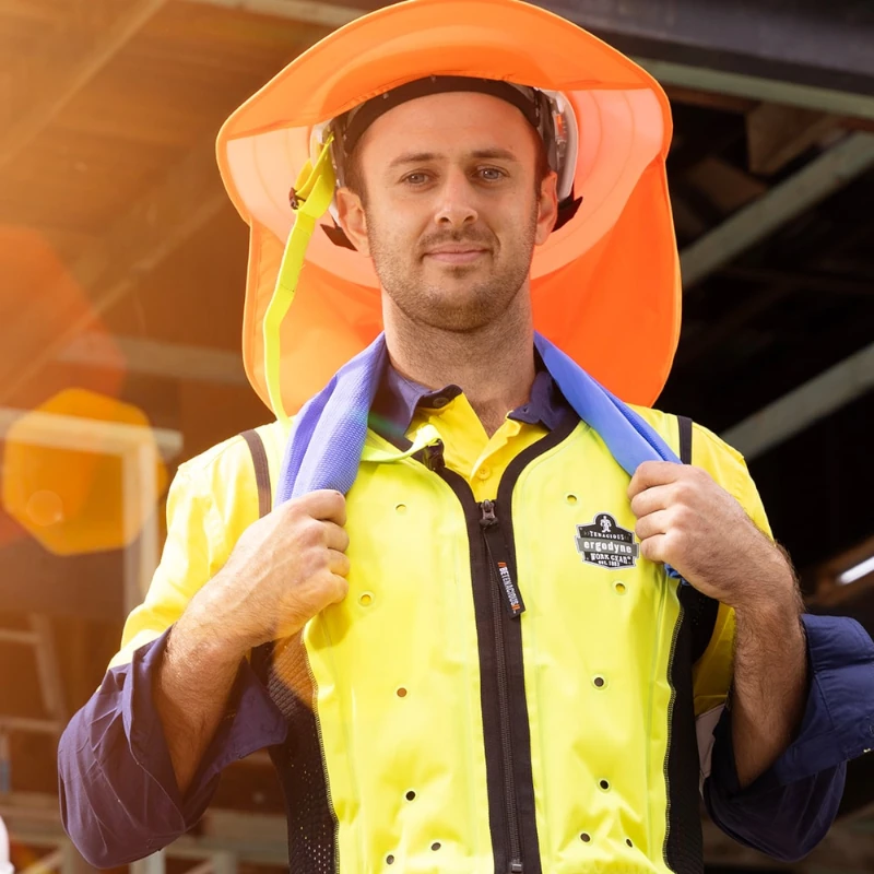 Construction worker in high-visibility cooling vest and brim hat wearing Ergodyne PPE for sun protection.