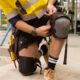 Tradesperson adjusting Ergodyne Proflex 360 knee pads while kneeling on construction site floor.