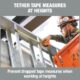 Construction worker using Ergodyne tethered tape measure to prevent drops while measuring at height.