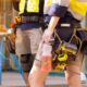 Worker holding a Sqwincher bottle with red electrolyte drink while wearing tool belt on construction site.