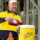 Worker in high-vis uniform pouring Sqwincher liquid concentrate into a yellow cooler jug on-site.